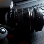 Close-up of a black DSLR camera with lens on a laptop keyboard.
